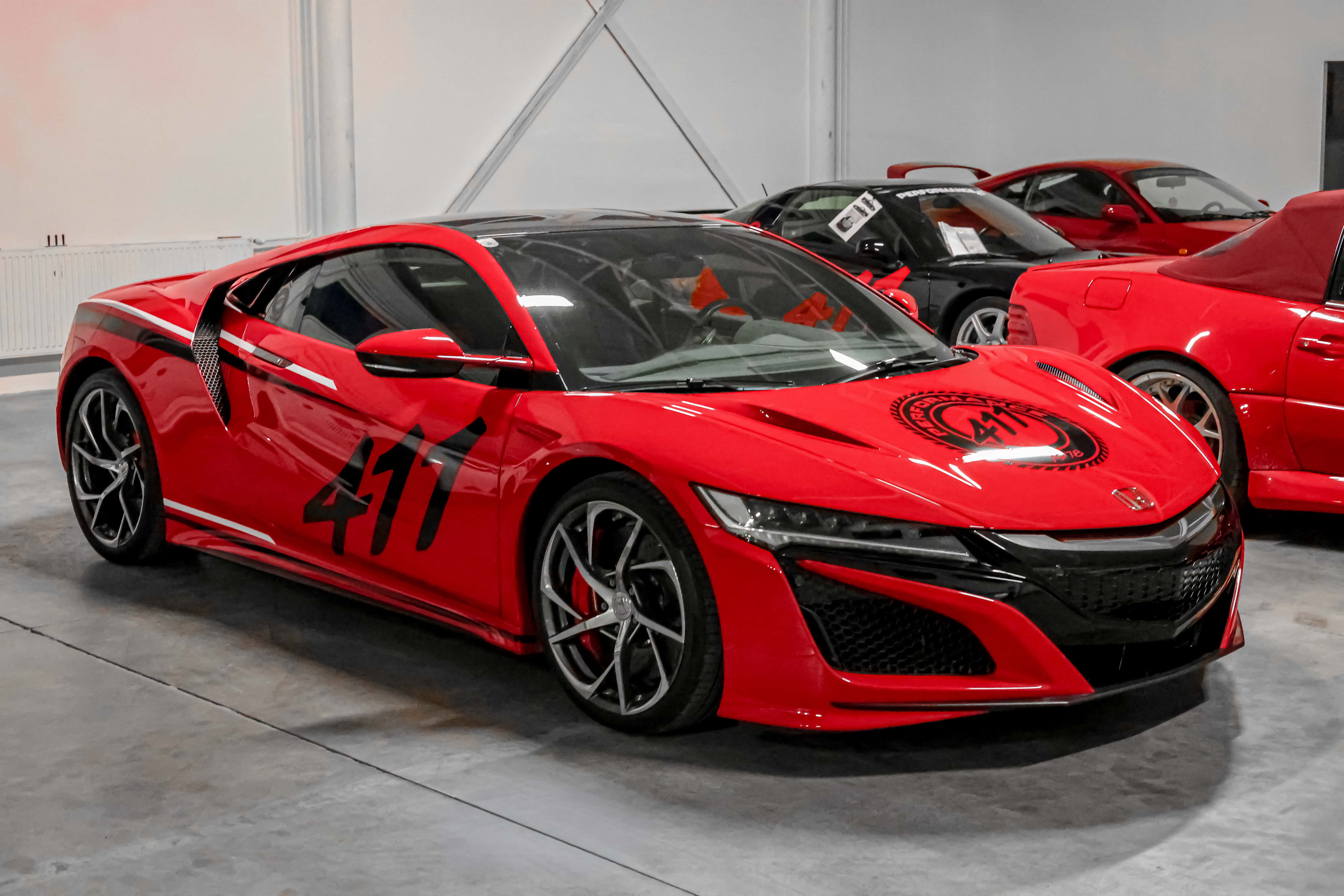 Pohľad z boku na červenú hondu nsx. Vozidlo polepené čierno-bielymi prvkami.