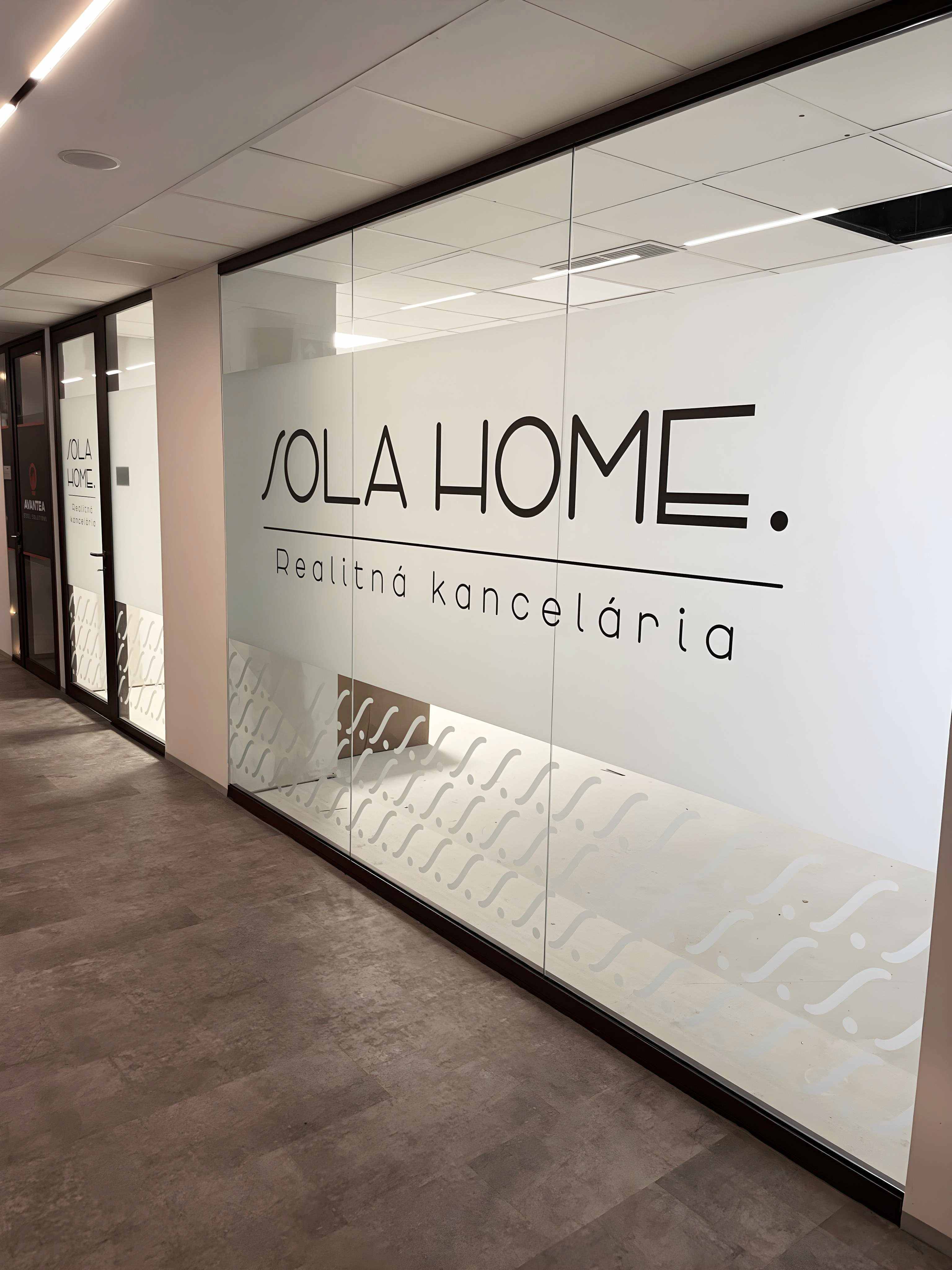 Pohľad z chodby na presklenú kanceláriu SOLA HOME s veľkým logom a matným dekoratívnym polepom.