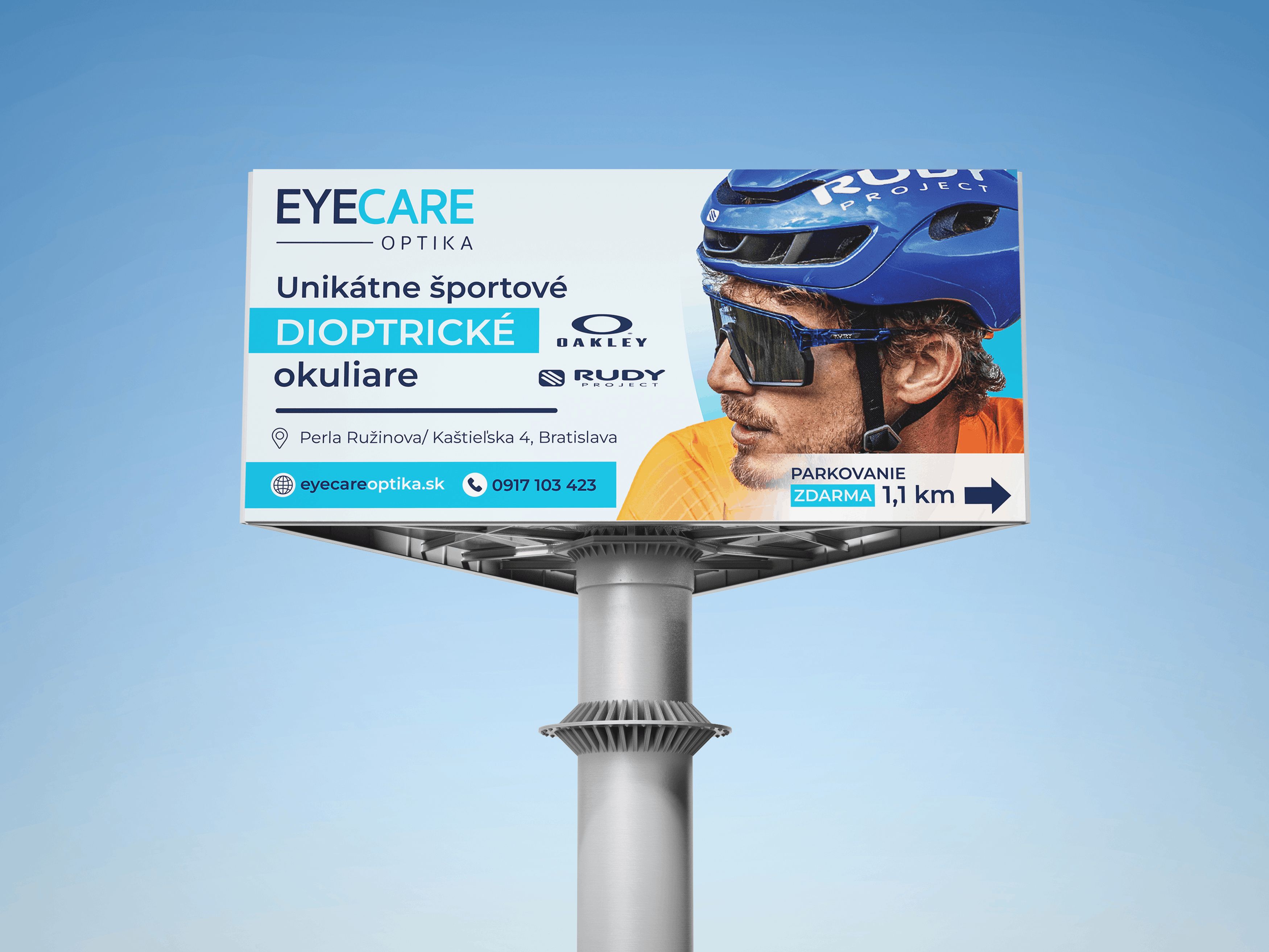 Reklamný billboard Eyecare Optika s fotografiou cyklistu v športových okuliaroch, modro-bielou grafikou a propagáciou dioptrických okuliarov Rudy.