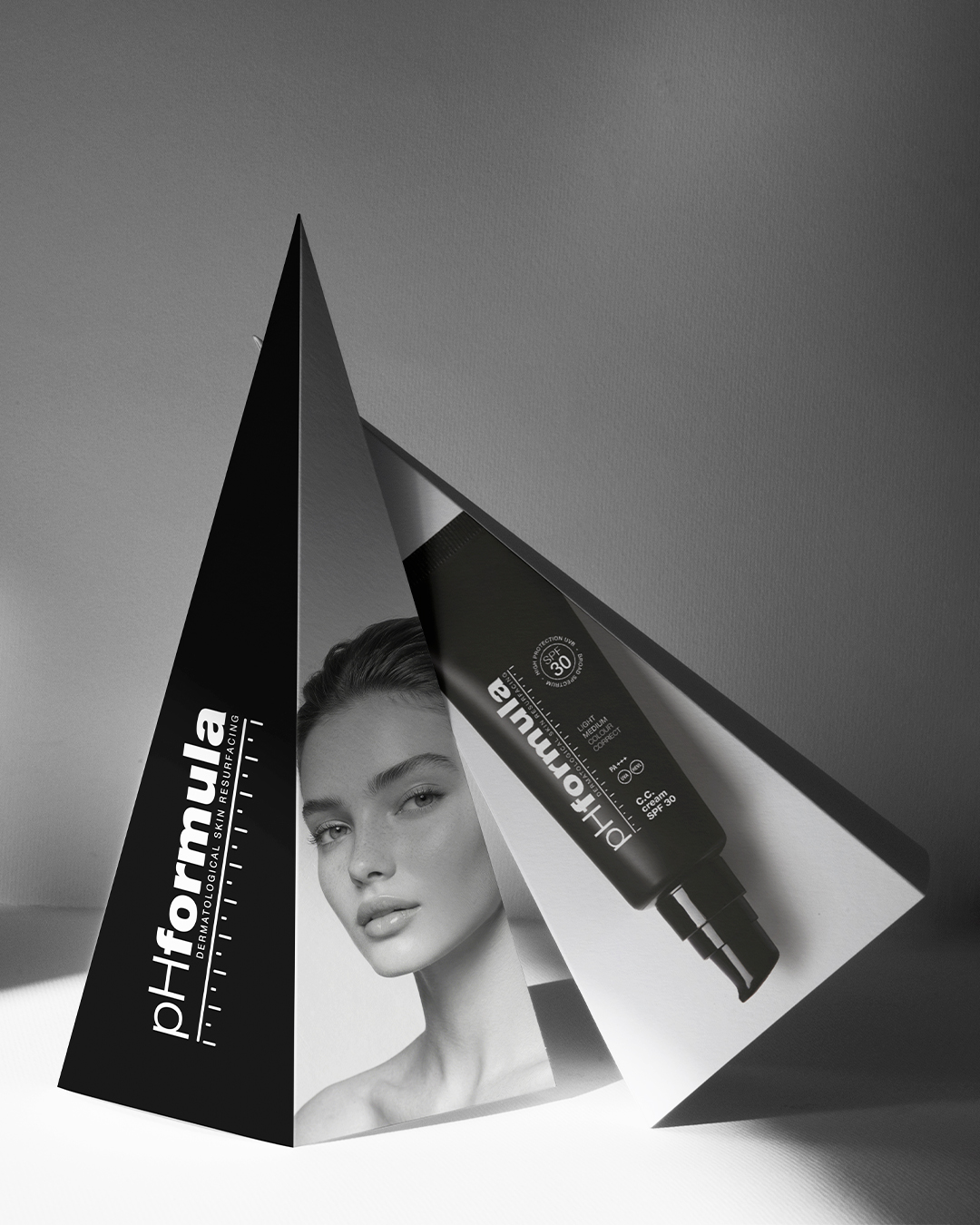 Čierny trojuholníkový prezentačný stojan pHformula s bielym logom, čiernobielou fotografiou modelky a vizuálom kozmetického produktu.