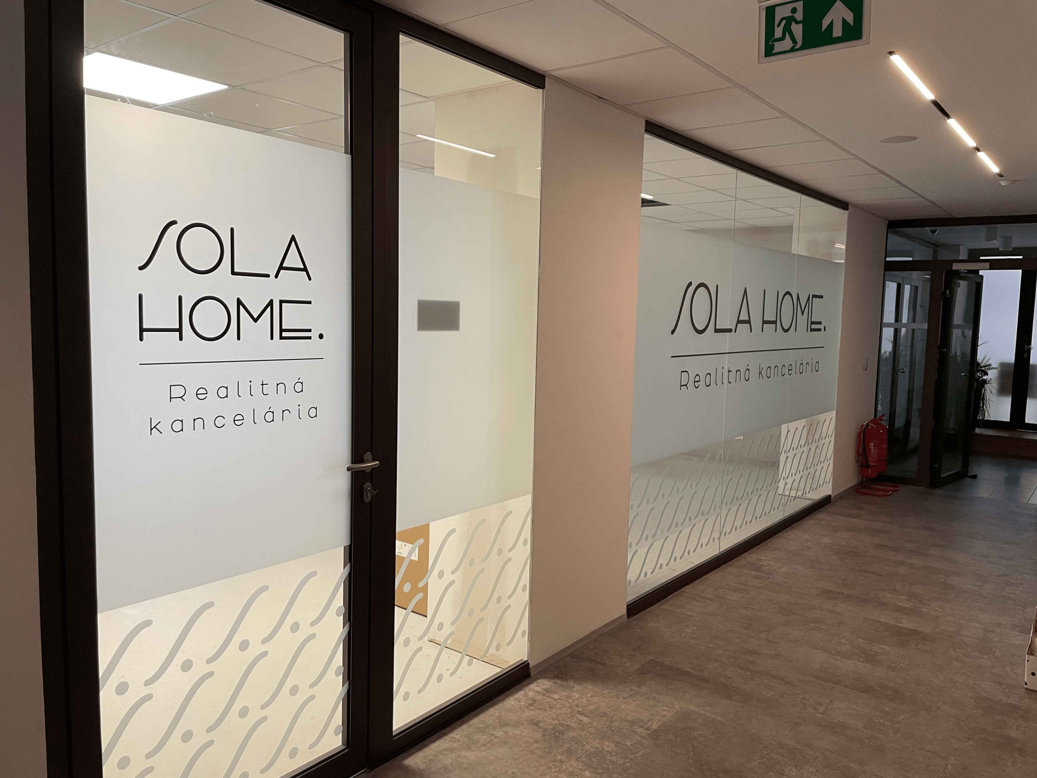 Realizovaný polep sklenených vstupných dverí realitnej kancelárie SOLA HOME s čiernym logom, matnou fóliou a dekoratívnym vzorom.